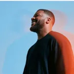 Man smiling with his eyes closed against a blue sky