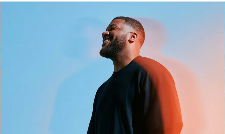 Man smiling with his eyes closed against a blue sky